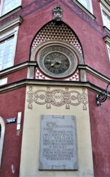 Narożny portal kamienicy Rynek 15, róg Zapiecka. Na narożniku zegar wg projektu Jerzego Brabandera i Zygmunta Kropisza, wykonany w 1953 roku przez Mieczysława Jarnuszkiewicza oraz tablica marmurowa upamiętniająca odbudowę Rynku Starego Miasta. Narożny portal kamienicy Rynek 15, róg Zapiecka